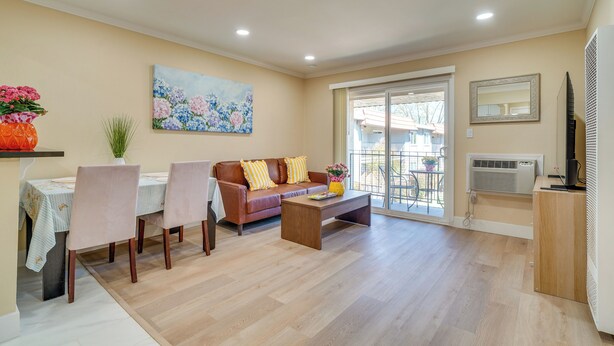 A living room with a sofa, coffee table, dining table with chairs, a painting, and a sliding glass door leading to an outdoor area. - Walkable Pleasanton Condo Near Downtown w/ Balcony (Pleasanton)