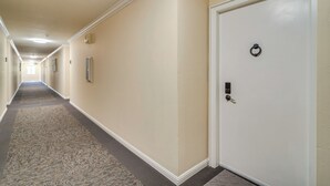 A hallway with a carpeted floor, a white door with a keyhole, and a wall-mounted light fixture. - Walkable Pleasanton Condo Near Downtown w/ Balcony (Pleasanton)