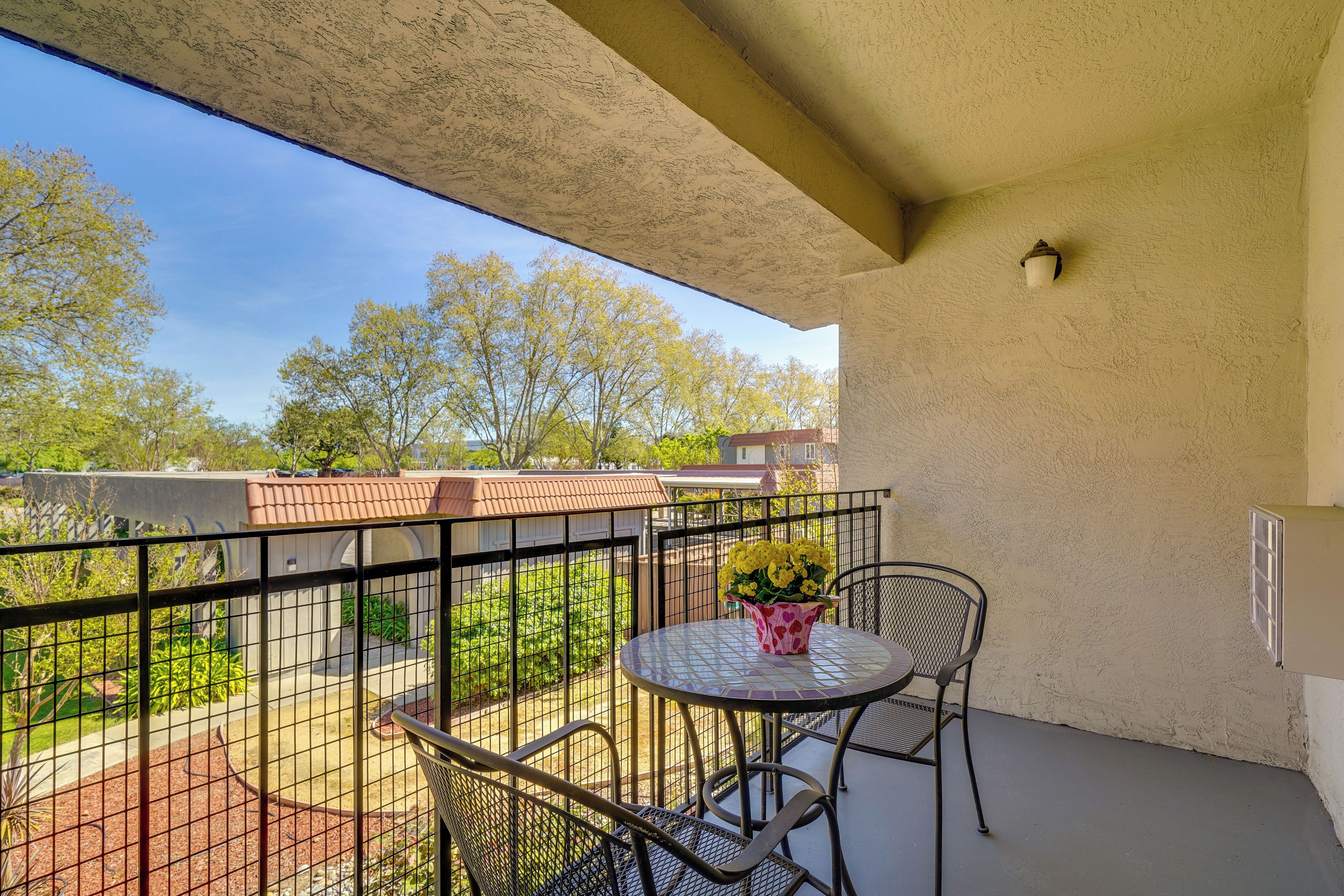 Un balcon avec une table et des chaises, un pot de fleurs et une vue sur les arbres et les bâtiments.