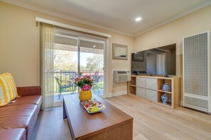 A living room with a sofa, a coffee table with a tray, a TV, a large window with curtains, and a balcony.