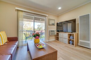 Un salón con sofá, una mesa de centro con bandeja, televisor, ventana grande con cortinas y balcón.