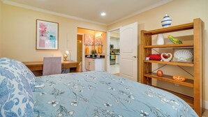 Een slaapkamer met een bed, een bureau, een stoel, een boekenkast en een keuken op de achtergrond.