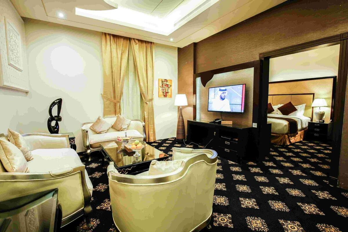 A hotel room with a sofa, a coffee table, a TV, a bed, and a patterned carpet.