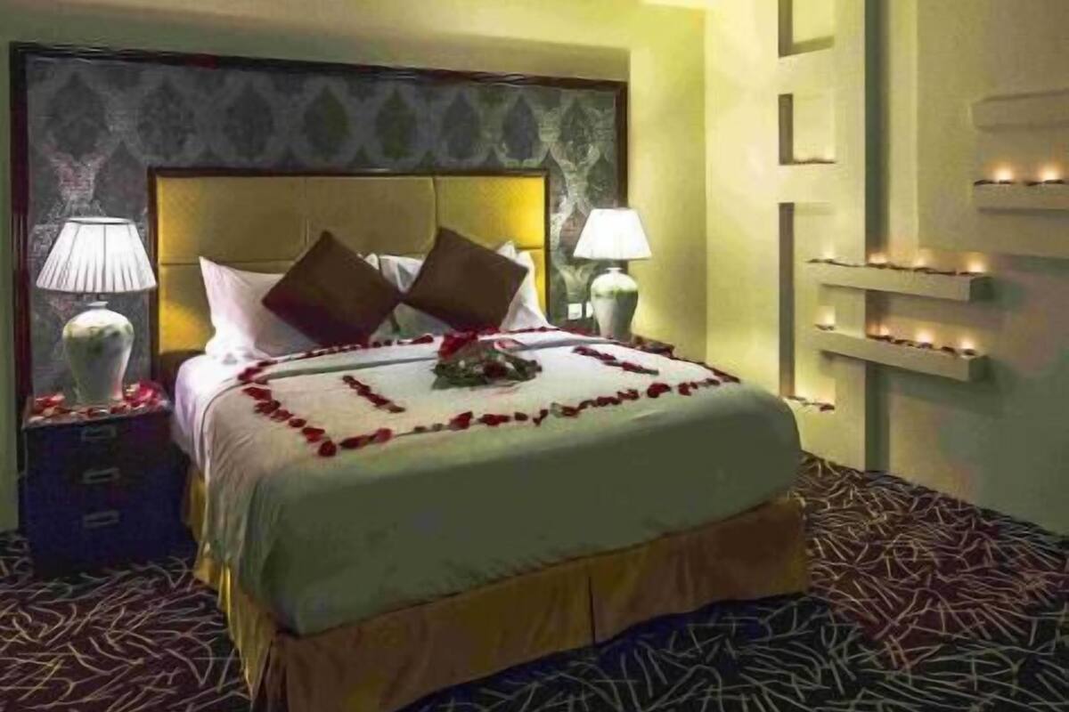 A hotel room with a large bed, two bedside tables, a decorative headboard, and a wall-mounted light fixture.