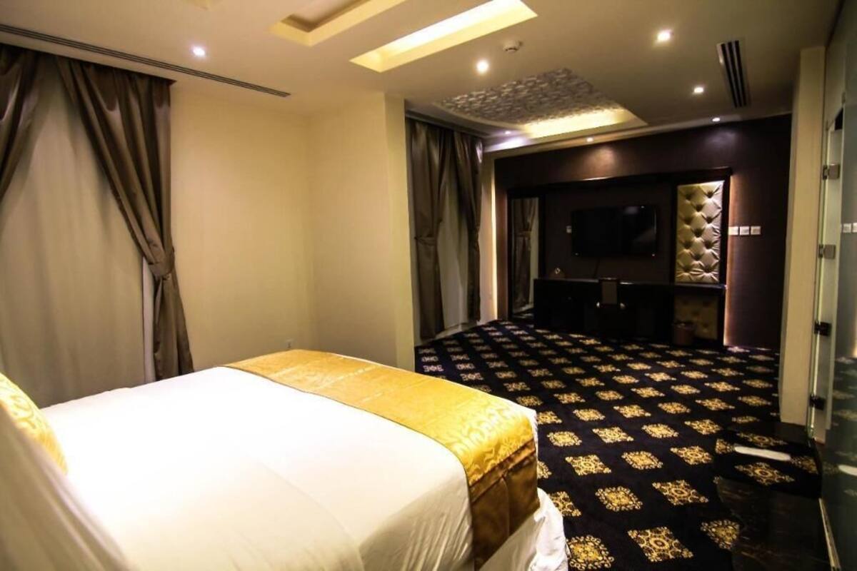A hotel room with a bed, a television, a seating area, and a patterned carpet.