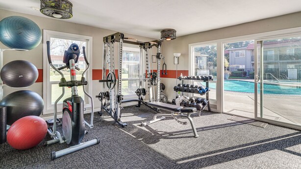 Academia com equipamentos de ginástica, piscina e vista para o exterior.