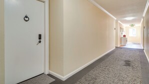 Um corredor com piso revestido de carpete, uma porta branca com puxador circular e um interruptor de luz na parede.