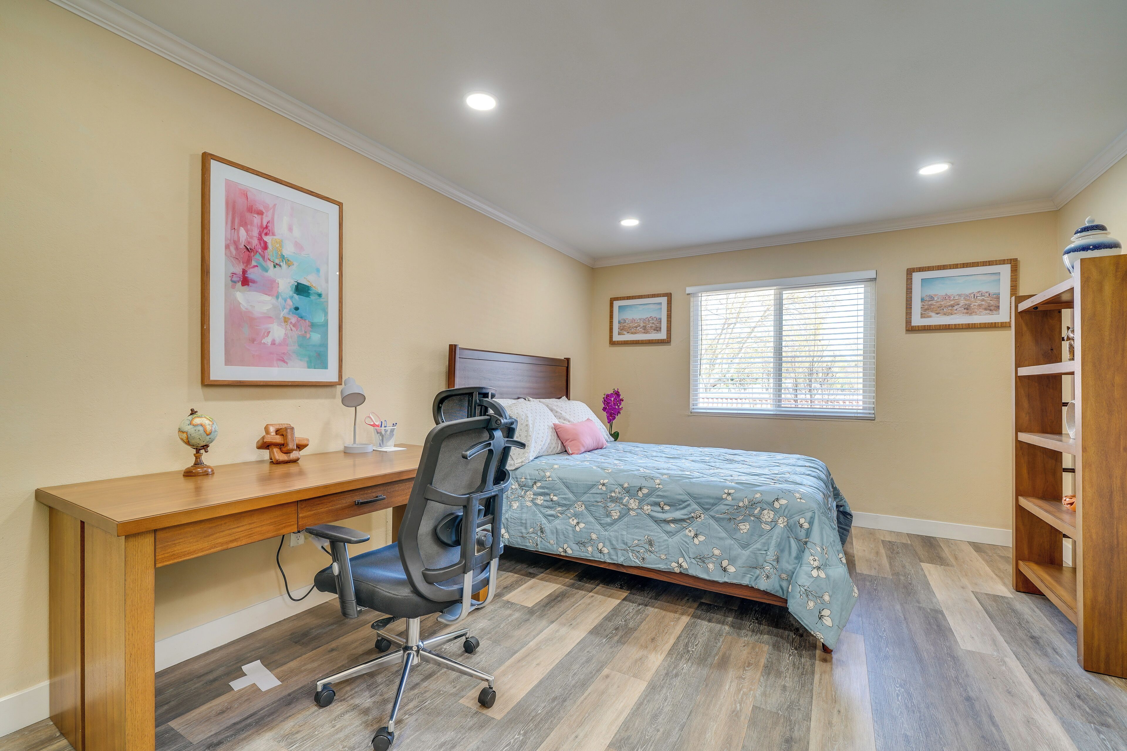 A bedroom with a bed, desk, chair, and shelving unit.