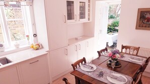 Ein Essbereich mit Holztisch, gedecktem Tisch für vier Personen, weißen Schränken, einem Fenster mit Gartenblick und einem Gemälde an der Wand.