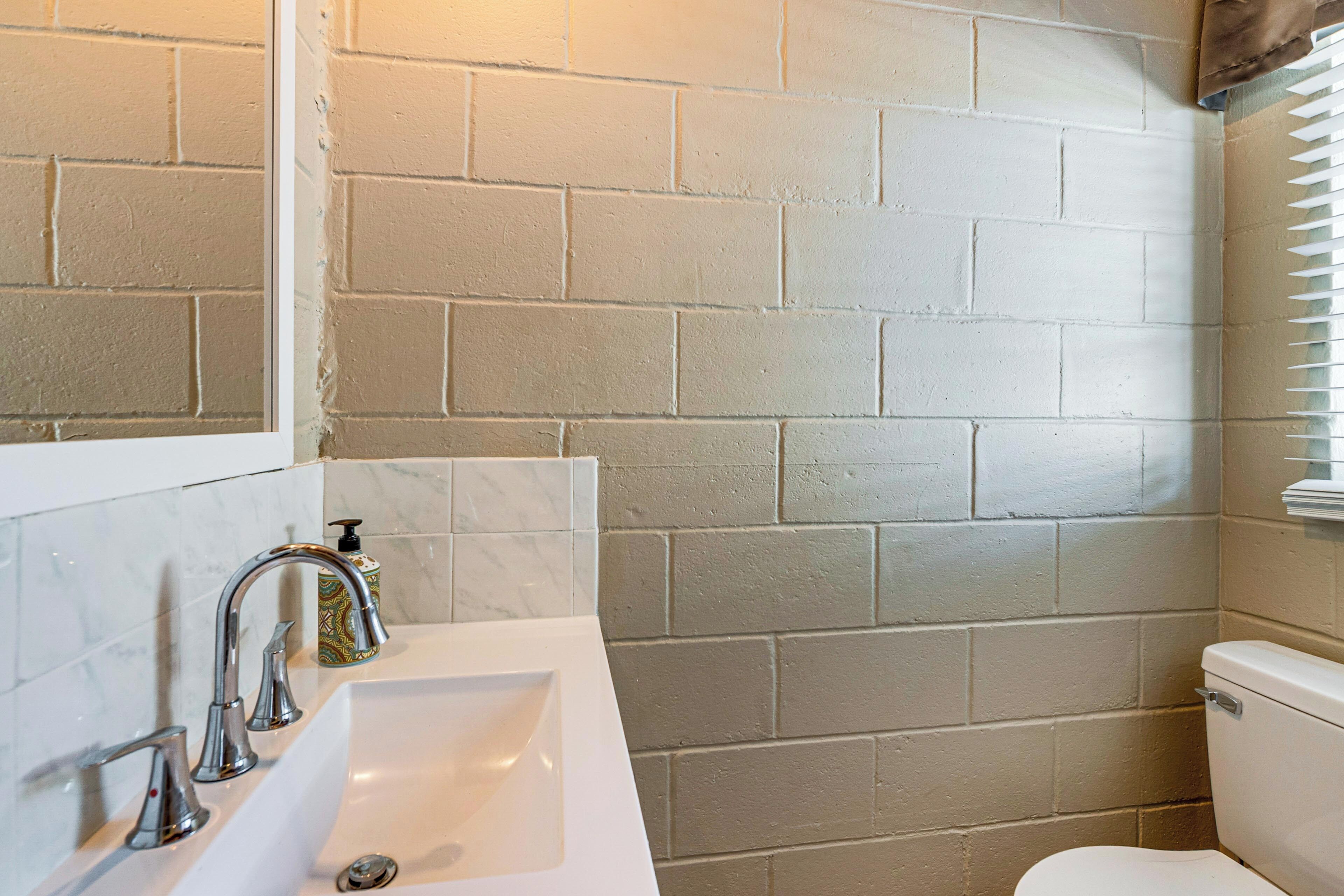 Un baño con un lavamanos blanco, dos grifos, un inodoro y una pared con azulejos.