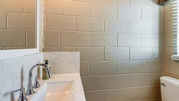 Un baño con un lavamanos blanco, dos grifos, un inodoro y una pared con azulejos.