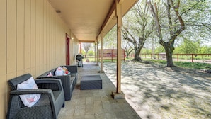 Un patio techado al aire libre con mobiliario de mimbre, una parrilla y vistas a árboles y una cerca.