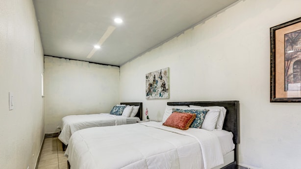 Habitación de hotel con dos camas, una lámpara en el techo, un cuadro en la pared y suelo de baldosas.