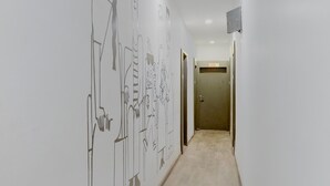 En hall med en vit vägg som pryds av abstrakta linjeteckningar, ett golv täckt av matta och en stängd dörr längst ner i hallen.