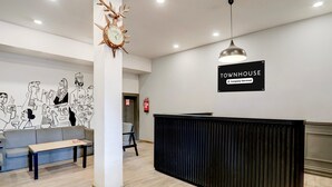 Ett väntrum med en svart receptionsdisk, en klocka, en soffa och en vägg prydd med en svartvit väggmålning.