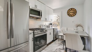 Een moderne keuken met roestvrijstalen apparatuur, witte keukenkastjes en een eethoek met een witte tafel en stoelen.