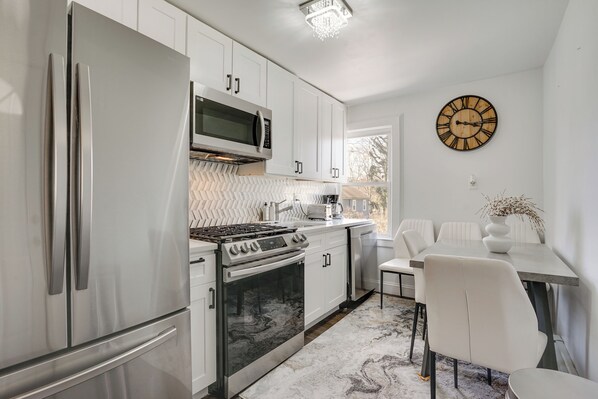 A modern kitchen with stainless steel appliances, white cabinetry, and a dining area with a white table and chairs. - Easy Access to Nyc! Sleek Suburban Apartment (Mamaroneck)