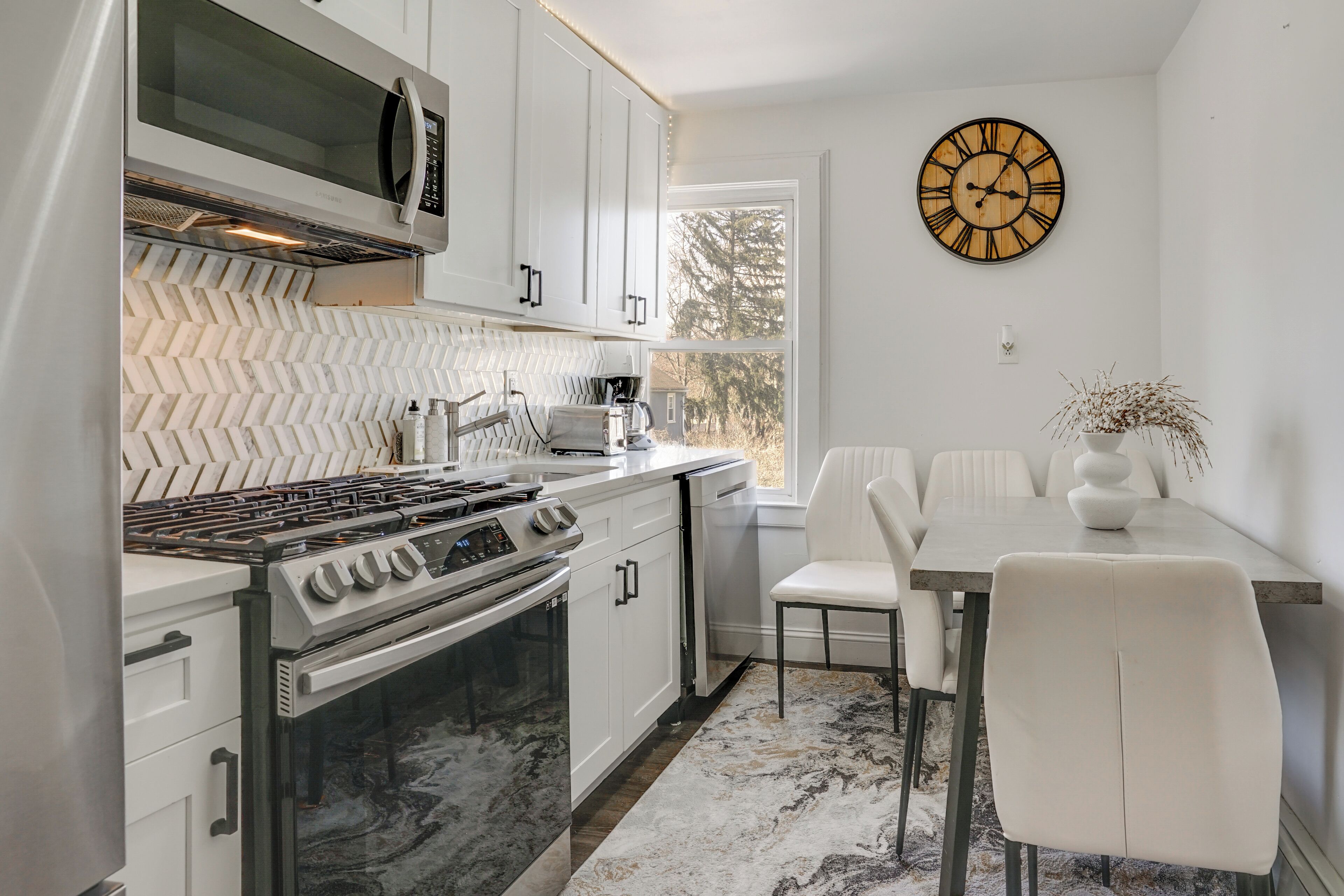 Cocina moderna con muebles blancos, estufa a gas, microondas y comedor con una mesa y sillas blancas.