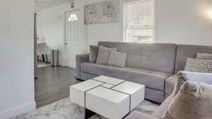 Een moderne woonkamer met een grijze bank, gestreepte kussens, een witte salontafel en een groot raam met jaloezieën.