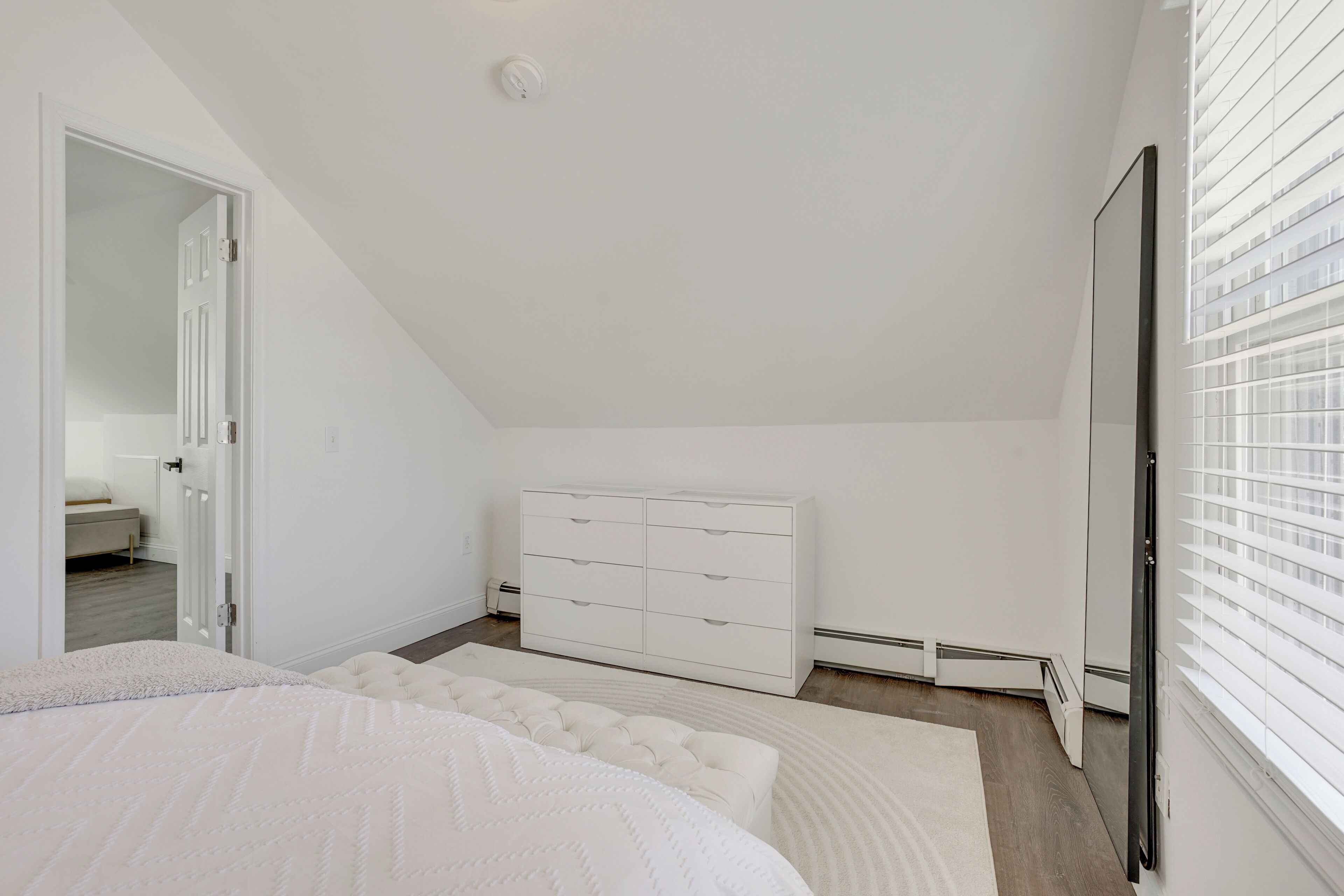 Ein Schlafzimmer mit Bett, Kommode, Kleiderschrank und einem Fenster mit Jalousien.
