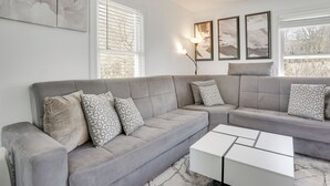 A modern living room with a grey sectional sofa, a white coffee table, and abstract wall art. - Easy Access to Nyc! Sleek Suburban Apartment (Mamaroneck)