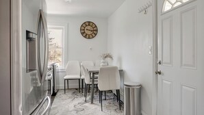 Een moderne keuken met een koelkast, een eettafel met stoelen, een klok aan de muur en een deur met raam.
