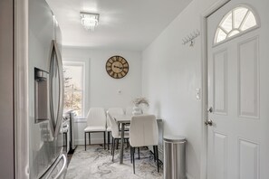 A modern kitchen with a refrigerator, a dining table with chairs, a clock on the wall, and a door with a window. - Easy Access to Nyc! Sleek Suburban Apartment (Mamaroneck)