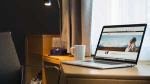 Um laptop sobre uma mesa de madeira com uma caneca branca, uma lâmpada e uma tomada.