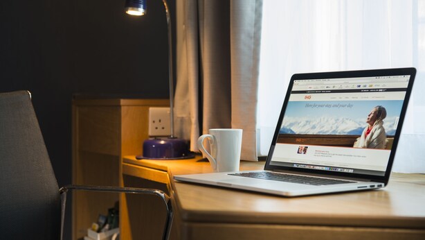 A laptop on a wooden desk with a white mug, a lamp, and a power outlet. - Holiday Inn Express Peterborough (Peterborough)