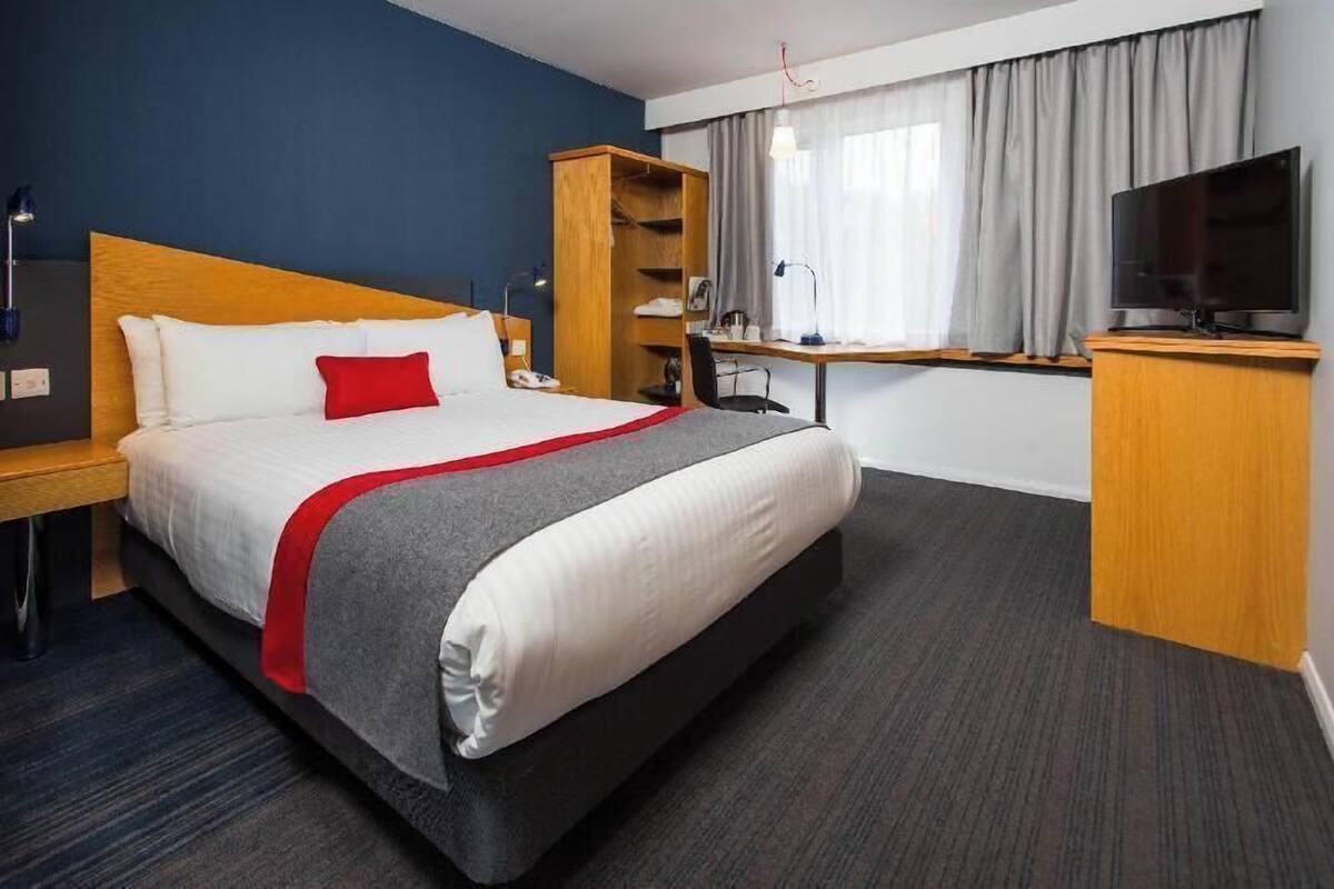 A hotel room with a bed, a desk, a TV, and a wardrobe.