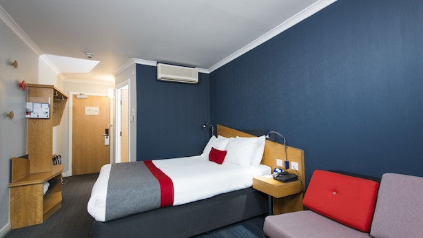 Quarto de hotel com cama, escrivaninha, cadeira, um laptop vermelho e um armário de madeira.
