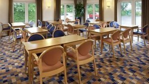 A hotel conference room with multiple tables and chairs, large windows, and a patterned carpet. - Holiday Inn Express Peterborough (Peterborough)