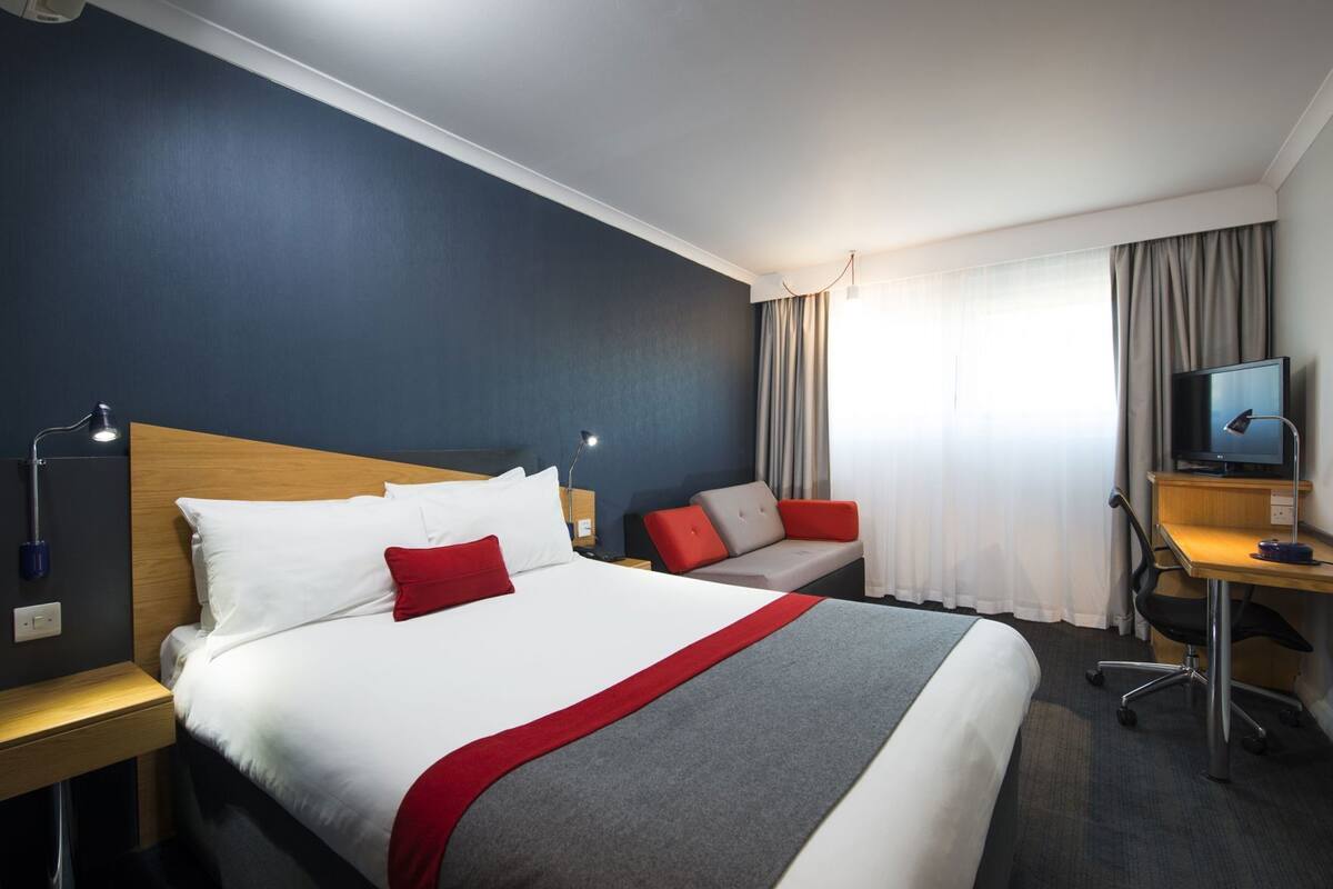 A hotel room with a bed, a desk, a television, and a chair.