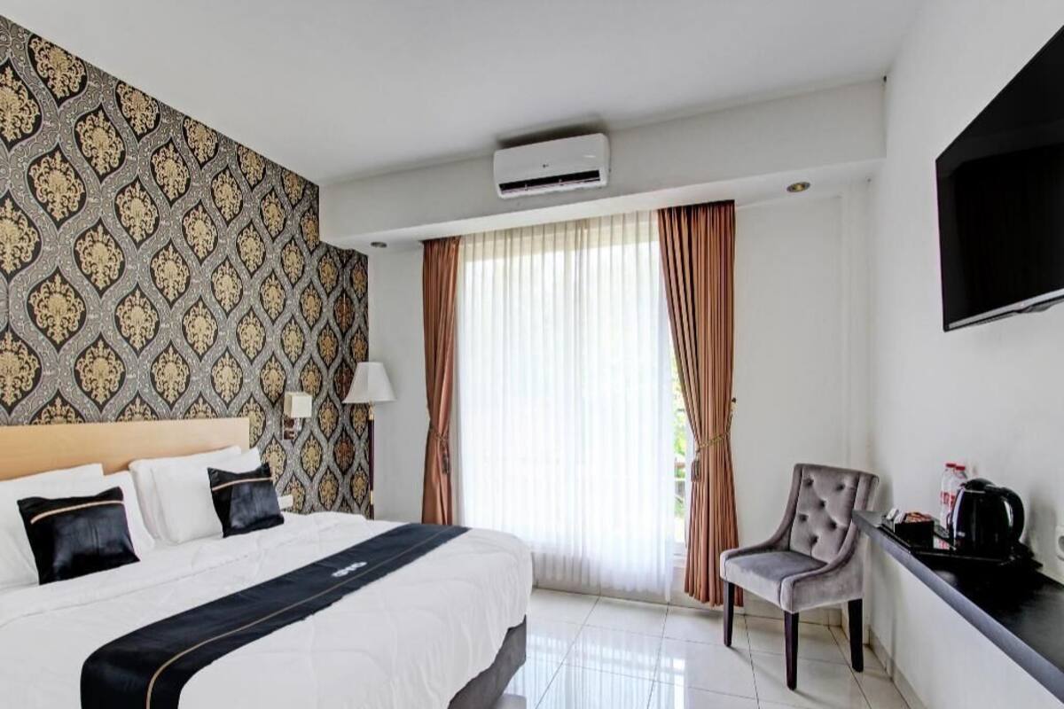 Une chambre d’hôtel avec un lit, une chaise, une télévision et une fenêtre avec des rideaux.