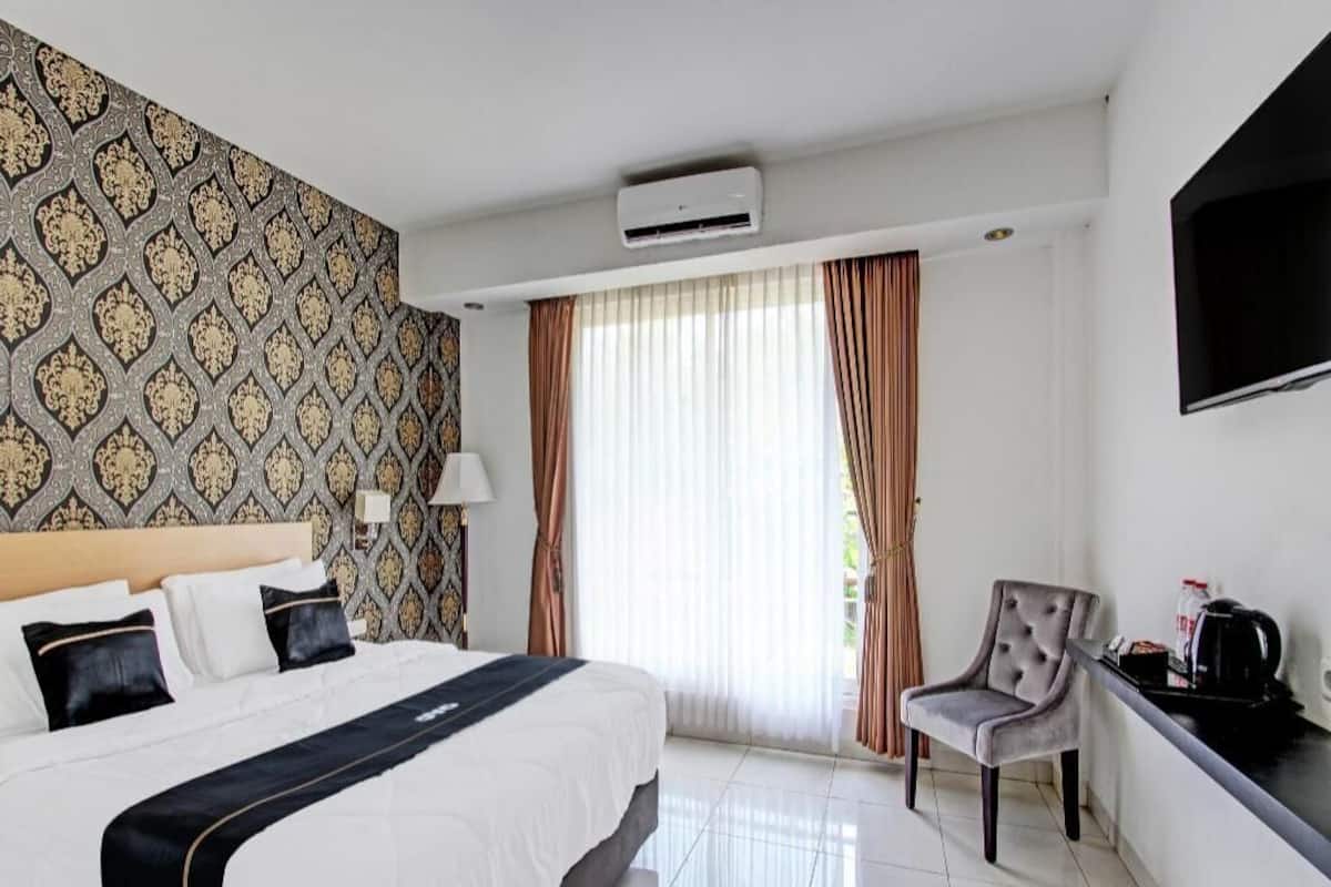 Quarto de hotel com cama, poltrona, televisão e janela com cortinas.