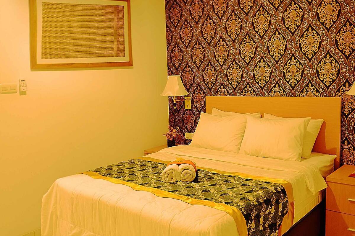 Une chambre d’hôtel avec un lit, une table de chevet, une lampe, un mur à motifs et un tableau encadré accroché au mur.