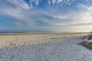 Uma praia arenosa com pegadas e vegetação rasteira.