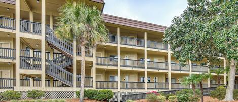 A multi-story hotel with balconies, a central staircase, and a well-maintained lawn.
