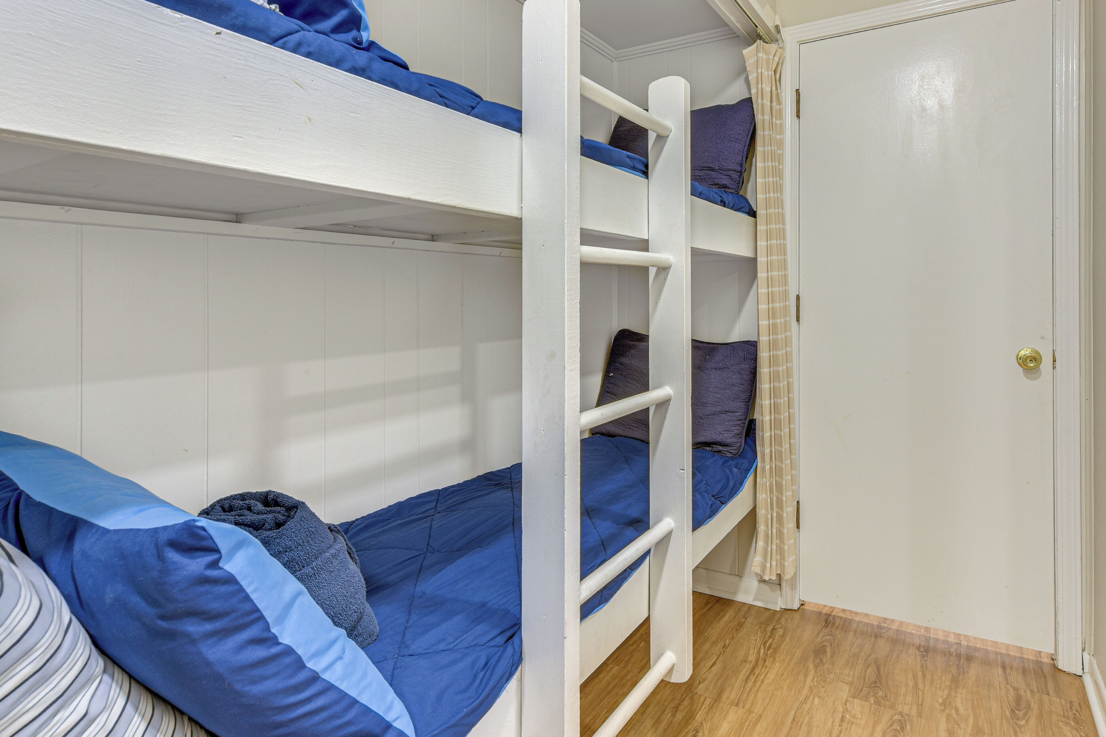 Habitació amb lliteres, terra de fusta, porta blanca i cortina.