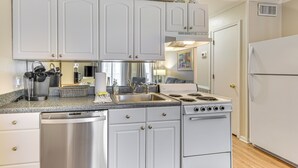 Une cuisine avec des armoires blanches, un lave-vaisselle en acier inoxydable, une cuisinière et un réfrigérateur.