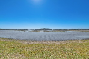A flat landscape with a water body and distant tree-covered land under a clear blue sky.