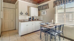 A kitchen with white cabinets, a dining table with chairs, and a window with blinds. - Paddle, Fish & Swim! Hernando Lake Cabin (Hernando)