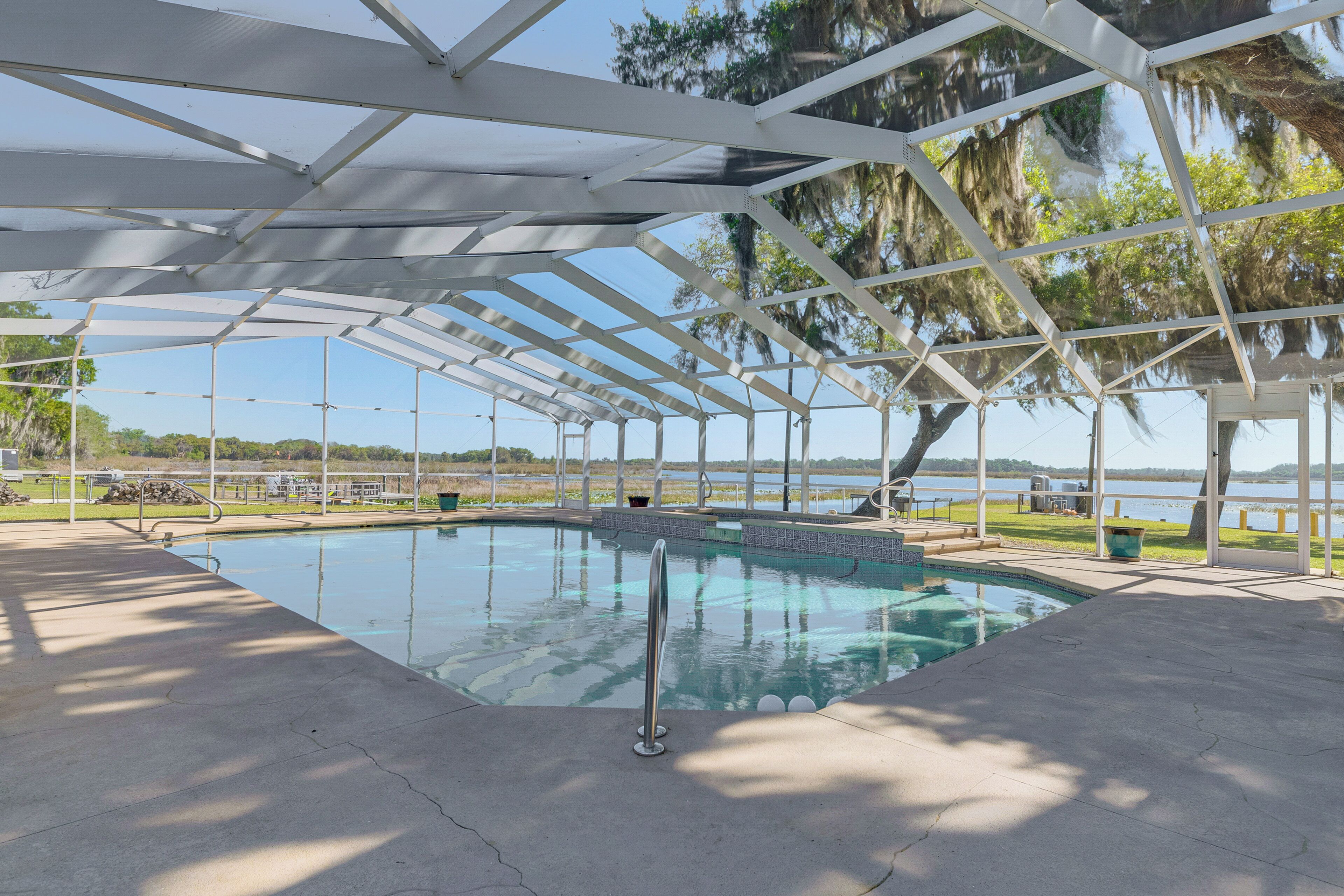 A covered swimming pool with a view of the lake and trees.