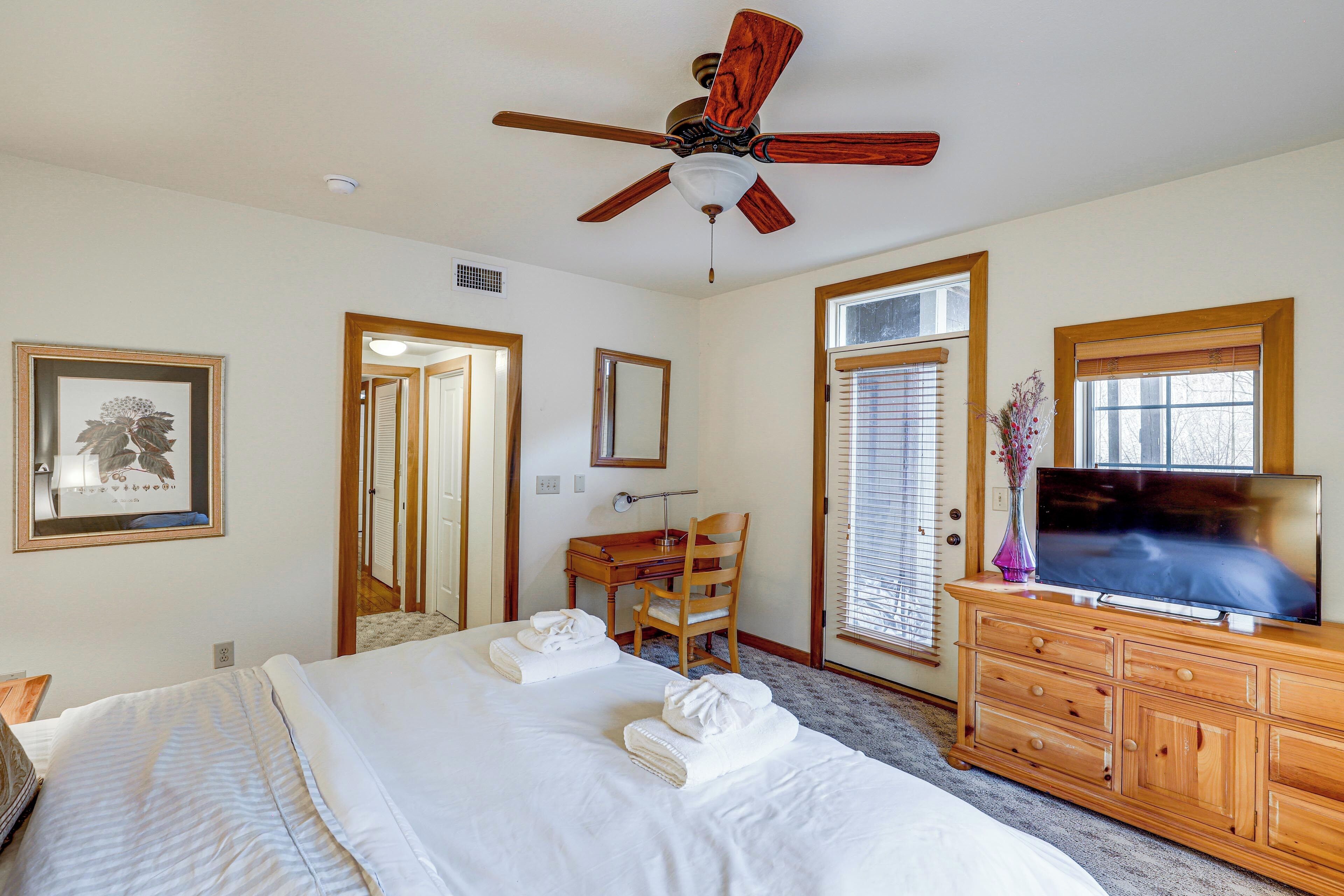 A hotel room with a bed, a desk, a chair, a television, and a ceiling fan.