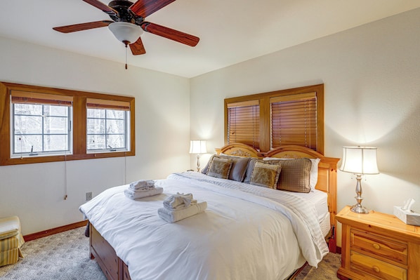 A bedroom with a bed, two bedside lamps, a wooden nightstand, a ceiling fan, and two windows with blinds. - Forest-view Balcony & Trail Access! Burnsville Gem (Burnsville)