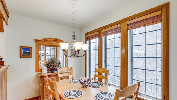 A dining room with a wooden table, chairs, a chandelier, and large windows with blinds. - Forest-view Balcony & Trail Access! Burnsville Gem (Burnsville)