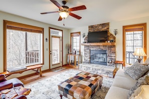 A living room with a stone fireplace, a ceiling fan, and a large window. - Forest-view Balcony & Trail Access! Burnsville Gem (Burnsville)