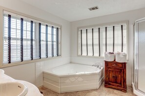 A bathroom with a bathtub, a vanity with a mirror, and two windows with blinds.