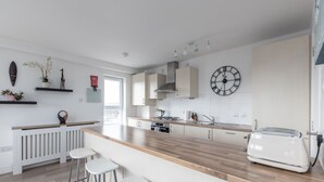 Een moderne keuken met een houten aanrecht, witte barkrukken, een witte koelkast en een klok aan de muur.