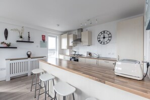 Eine moderne Küche mit einer Holzarbeitsplatte, weißen Barhocker, einem weißen Kühlschrank und einer Wanduhr.
